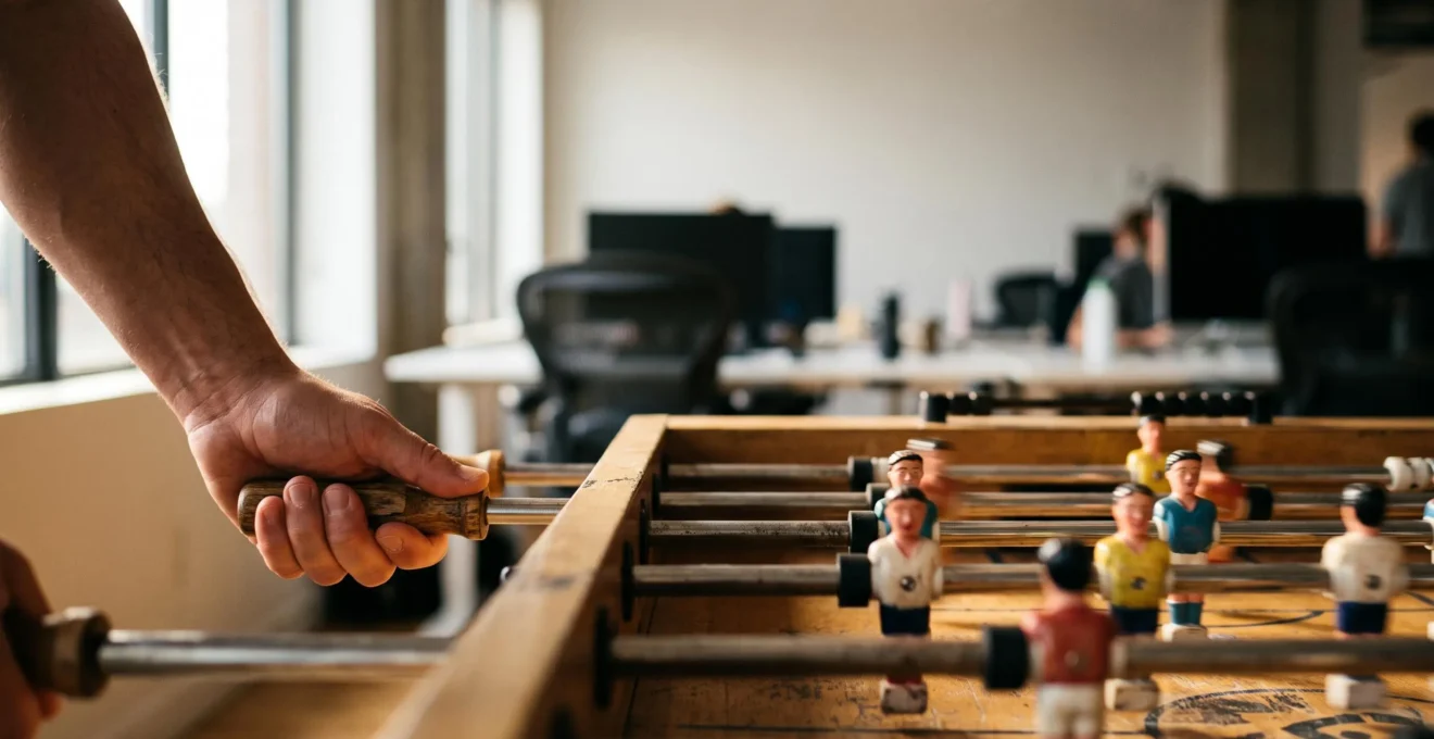 Employé en costume décontracté frappant une balle de baby-foot dans un espace de pause lumineux, symbolisant la coupure mentale en pleine journée de travail